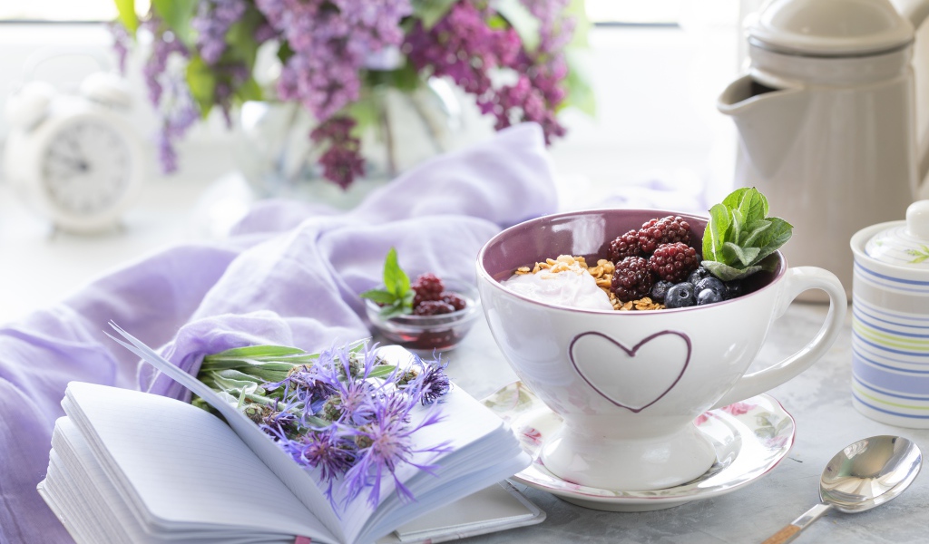 Мюсли с ягодами в чашке на столе с блокнотом и букетом сирени 