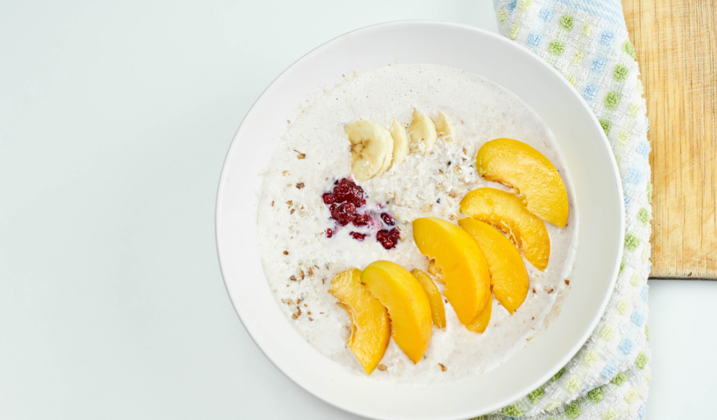 Мюсли с йогуртом в тарелке с кусочками банана и персика