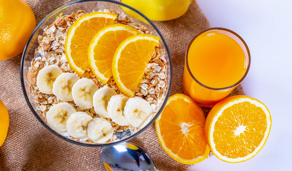 Овсяные хлопья в тарелке с кусочками банана и апельсина на столе с соком