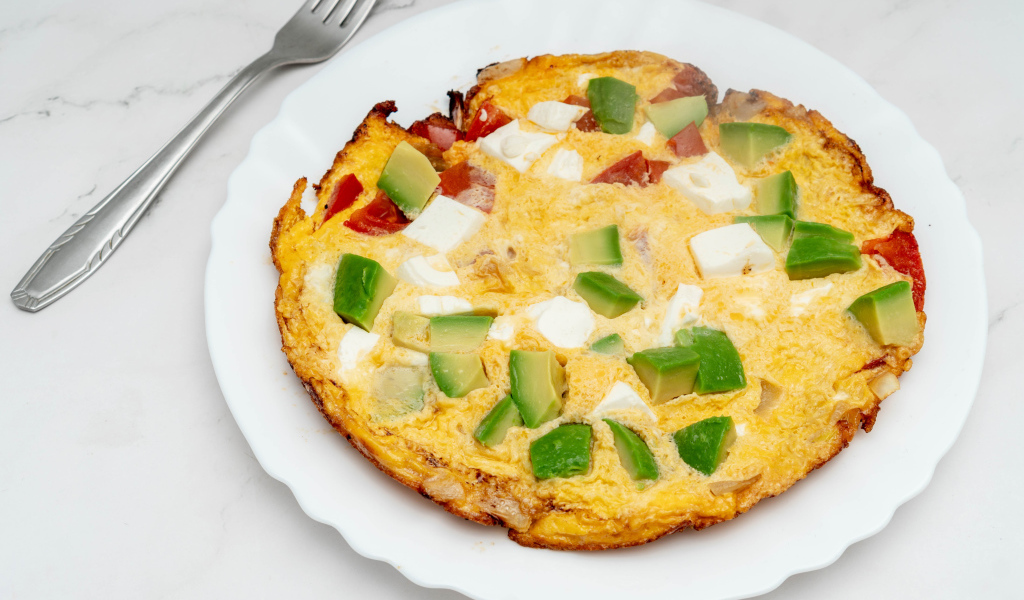 Омлет с авокадо и кусочками помидора на белой тарелке 