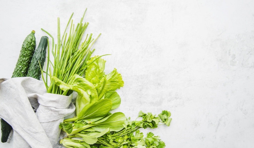 Зелень петрушки и лука, листья салата и свежие огурцы на белом фоне
