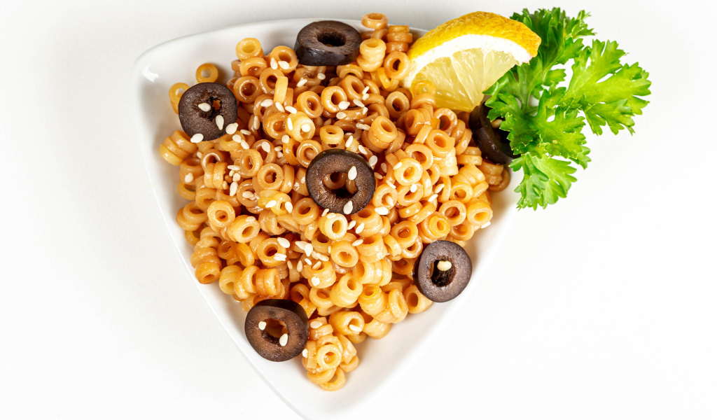 Макароны на тарелке с оливками и лимоном