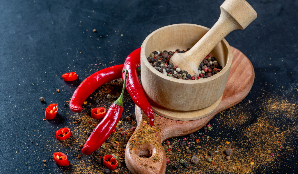 Перец горошком в ступке на столе с острым перцем