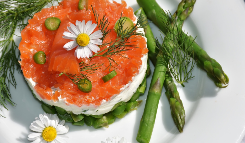 Салат с красной рыбой на тарелке со спаржей, укропом и цветами ромашки