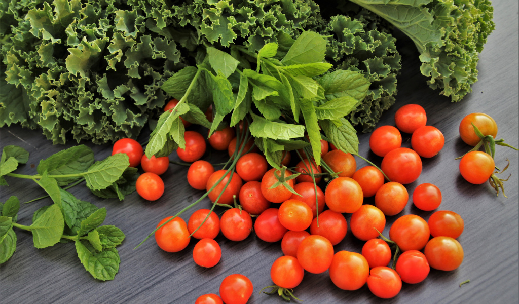 Красные мелкие помидоры на столе с зеленью 