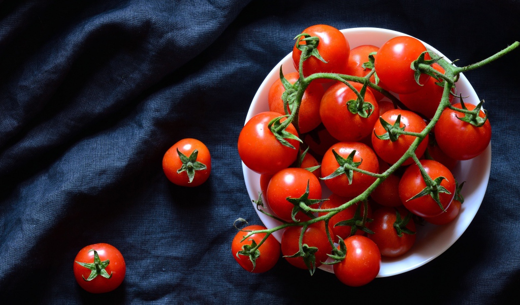 Красные помидоры в белой миске на черном фоне