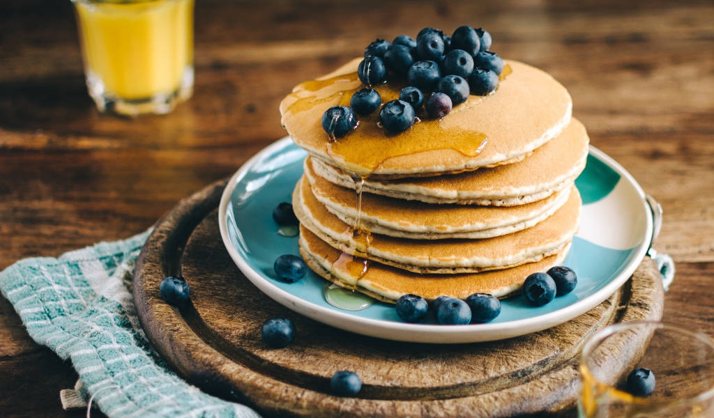 Румяные оладья на тарелке  с медом и ягодами черники 