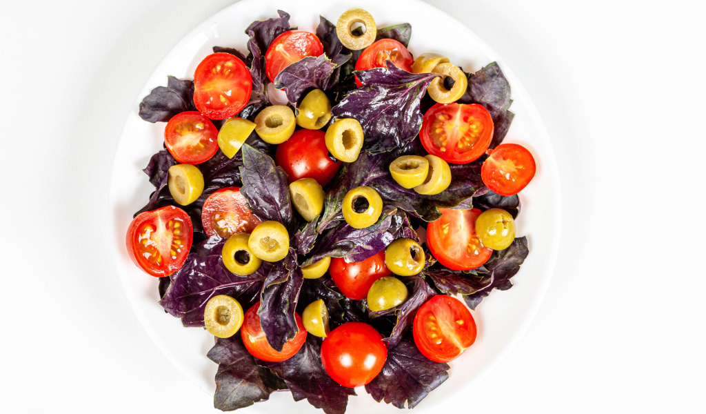 Салат с листьями базилика, помидорами и оливками на белом фоне