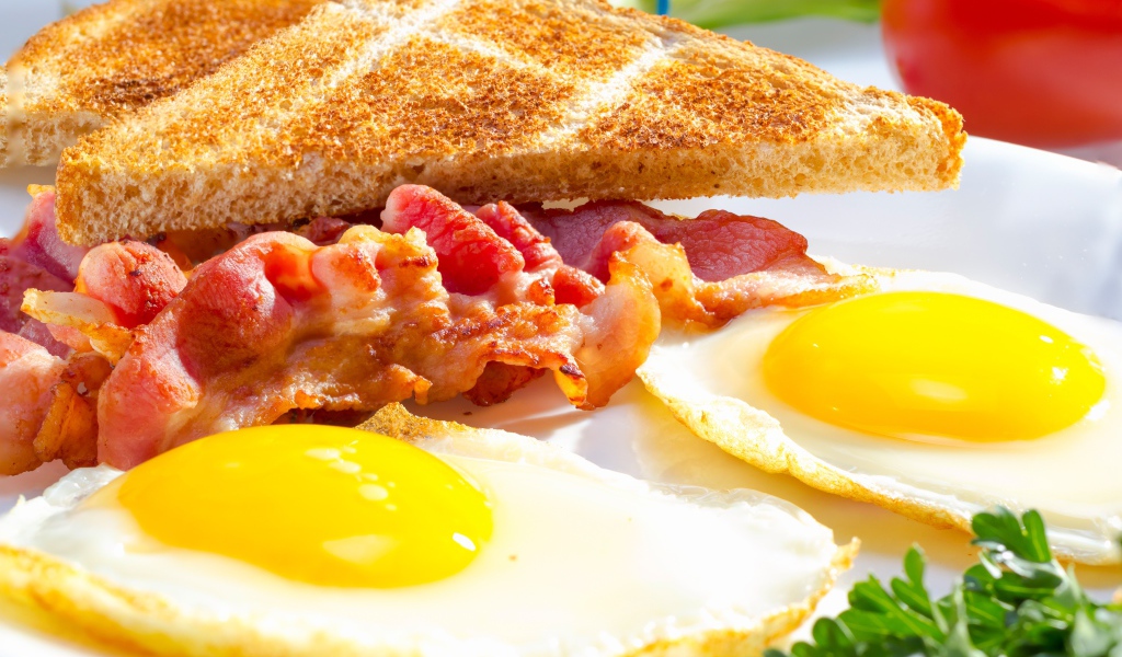 Яичница, бекон и гренки на завтрак на столе 