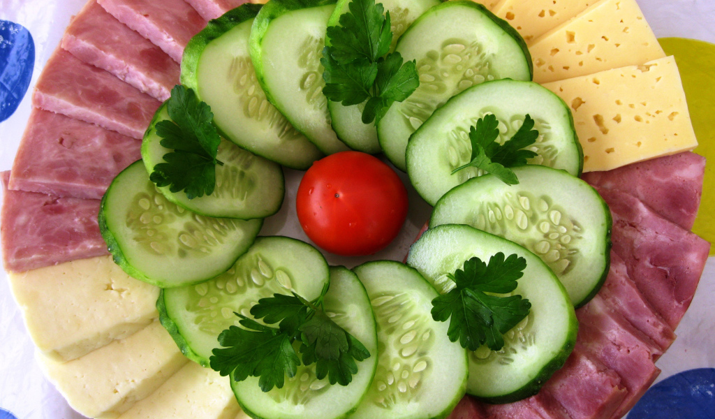 Сыр нарезанный, огурцы и ветчина на тарелке 