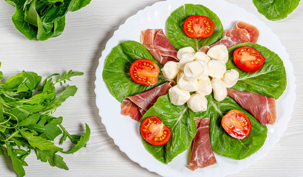 Кусочки ветчины на тарелке с сыром, помидорами и листьями салата