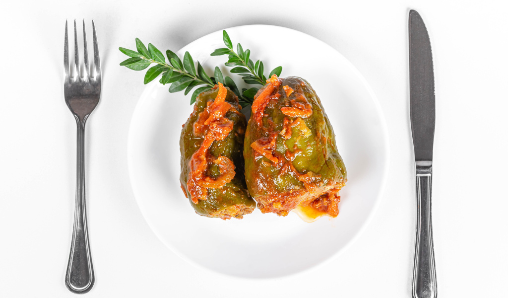 Фаршированный перец на белой тарелке со столовыми приборами