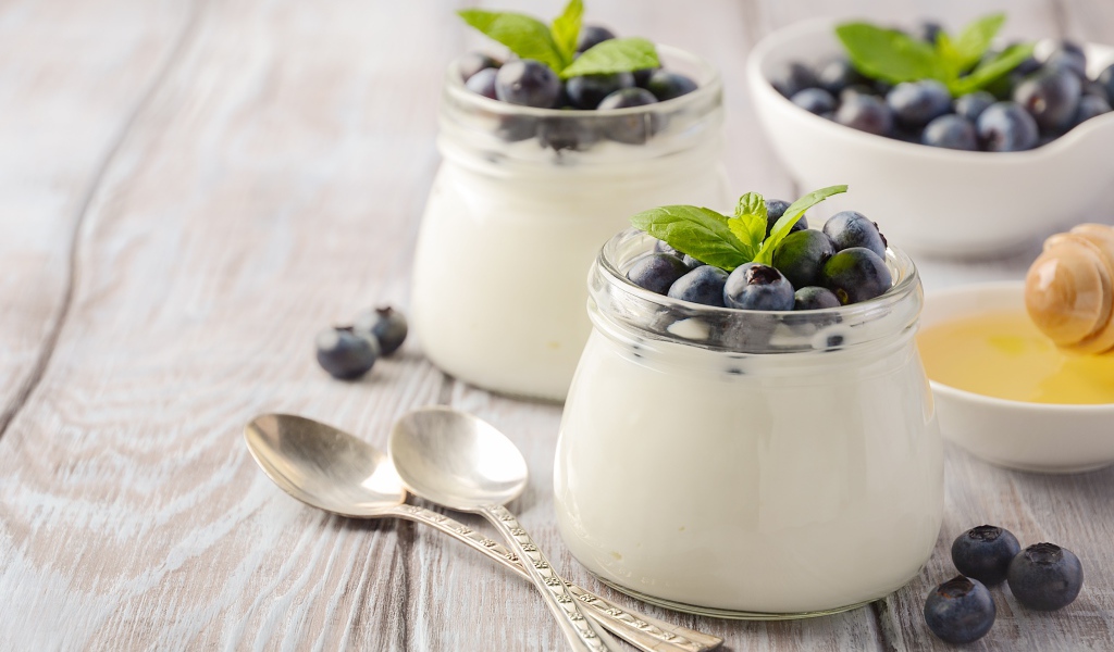 Йогурт в банках с ягодами черники на столе с ложками и медом