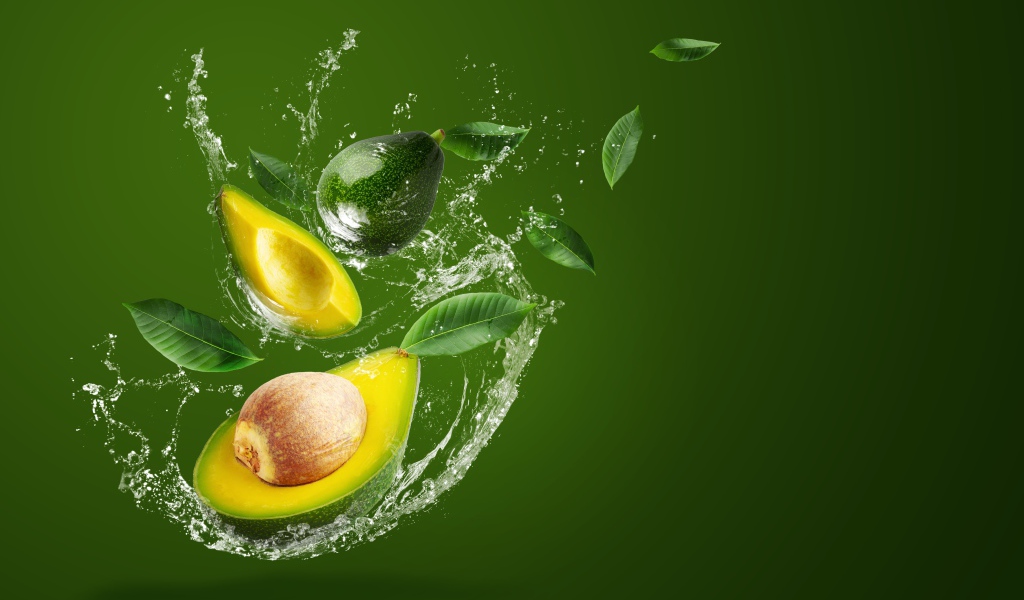 Авокадо в брызгах воды на зеленом фоне