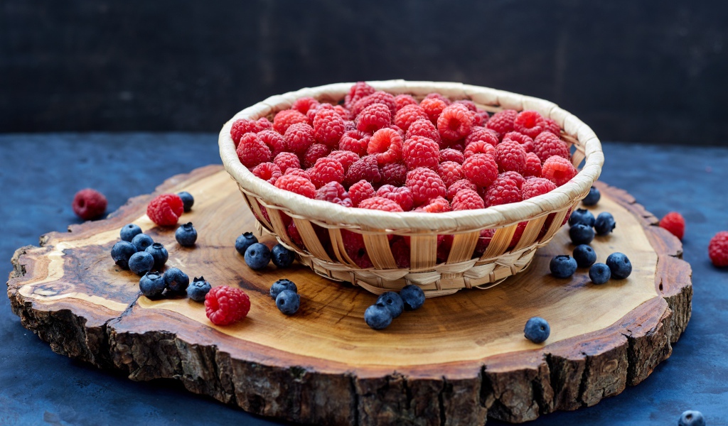 Корзинка с малиной на столе с ягодами черники