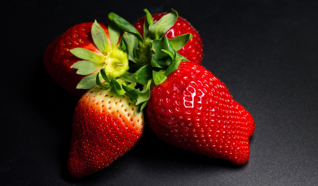 Четыре спелых красных ягоды клубники на черном столе 