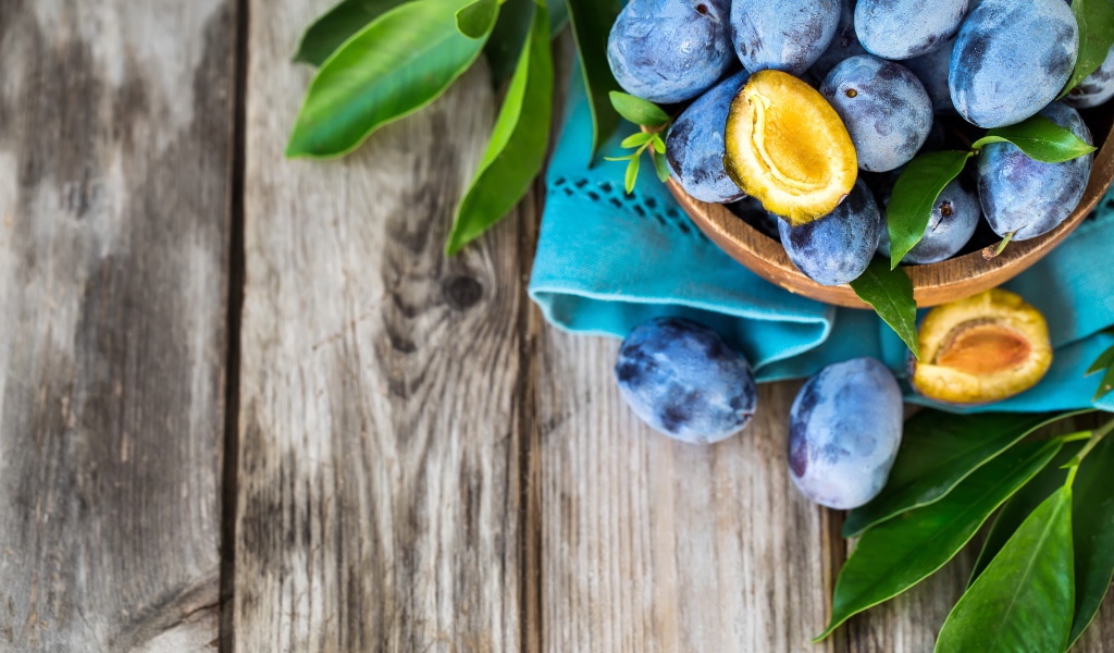 Свежие синие сливы с зелеными листьями на столе 
