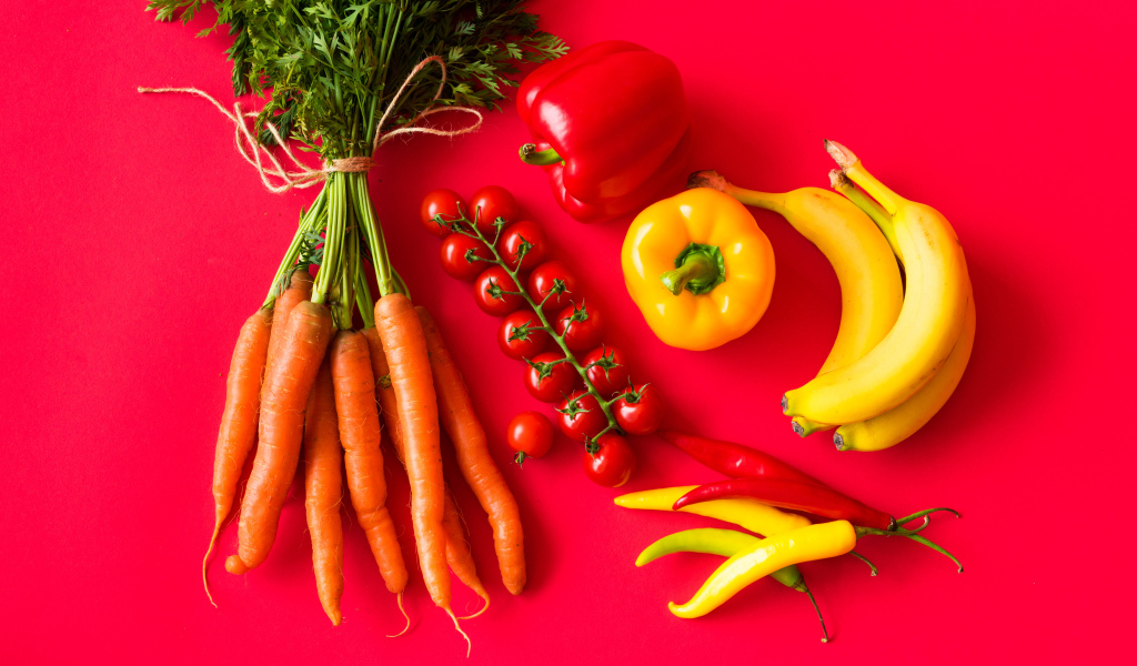 Свежие морковь, помидоры, перец и бананы на красном фоне