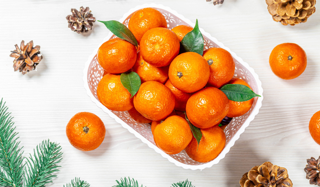 Много спелых мандаринов в белой корзинке на столе с шишками