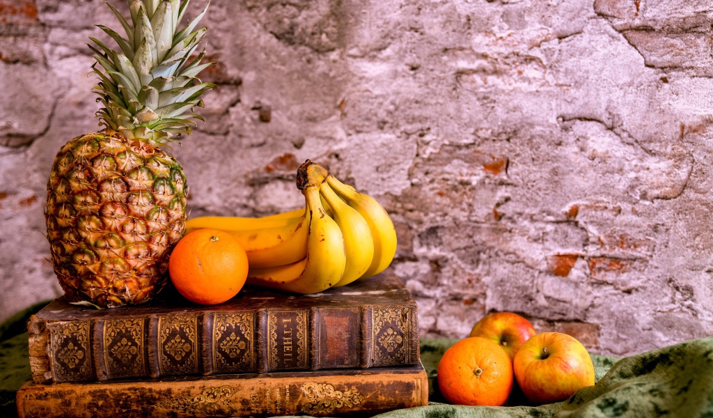 Апельсины, бананы, яблоки и ананас на столе со старыми книгами