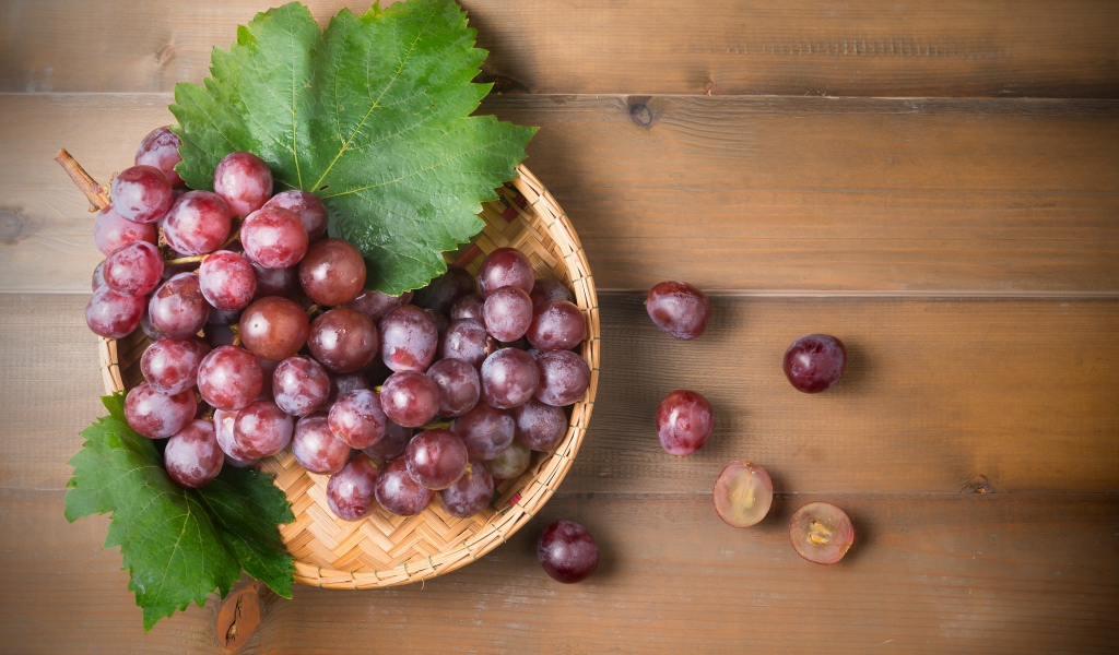 Розовый виноград с зелеными листьями на деревянном столе 