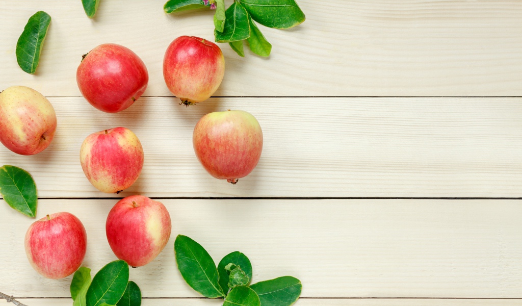 Красные яблоки с зелеными листьями на деревянном столе 