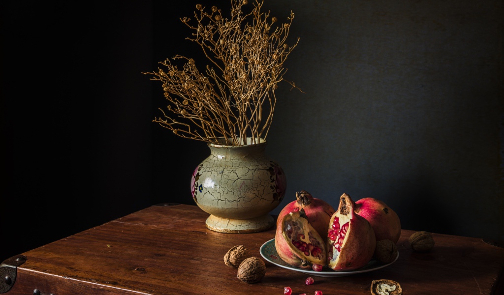Красный гранат на столе с грецкими орехами и сухой веткой в вазе