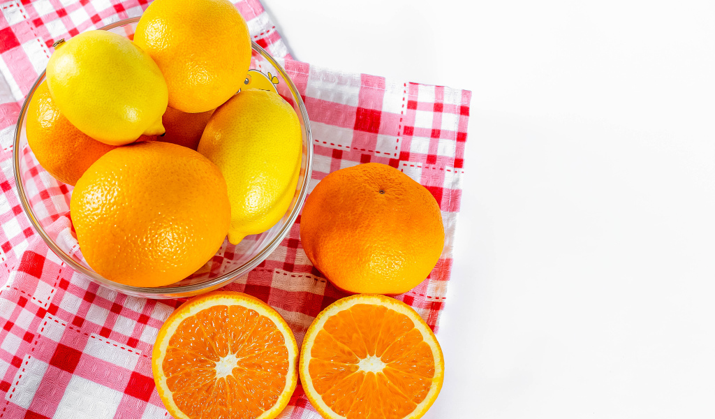 Спелые апельсины и лимоны в стеклянной миске на столе