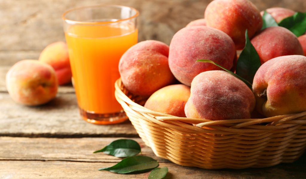 Спелые персики в корзине на столе с соком