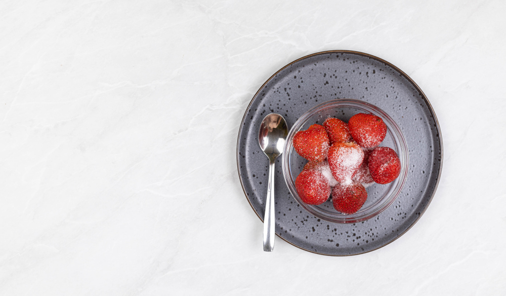 Спелая красная клубника в миске с сахаром на белом фоне