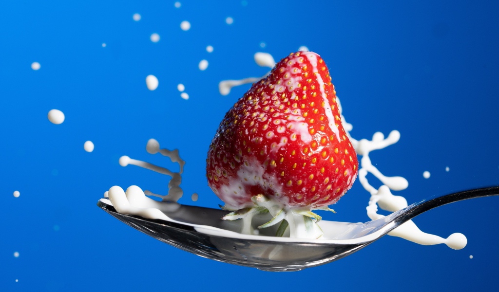 Спелая красная клубника в ложке молока на голубом фоне