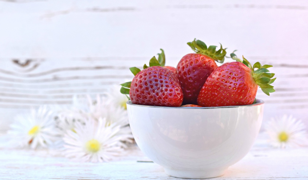Спелая клубника в белой миске на столе с ромашками