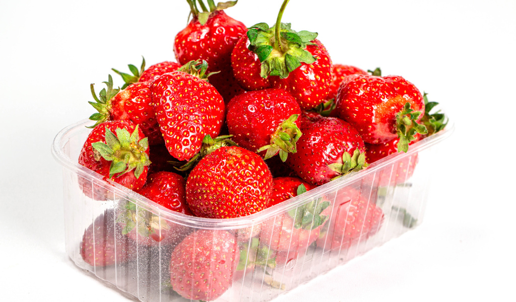 Спелая вкусная клубника в пластиковом контейнере на белом фоне