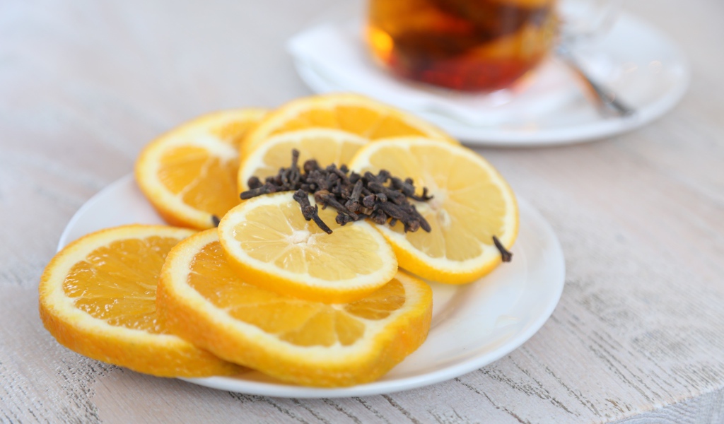 Нарезанный апельсин и лимон на тарелке с гвоздикой