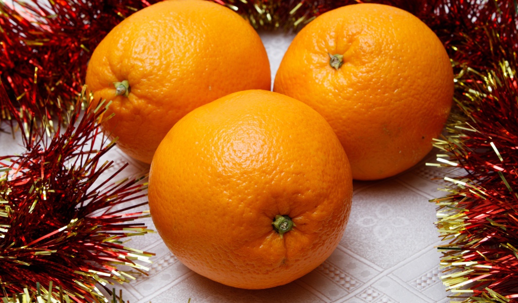 Три больших апельсина на столе с мишурой 