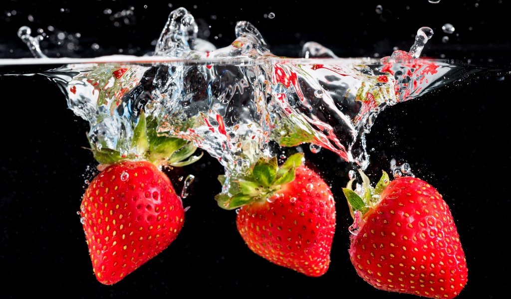 Три ягоды клубники в воде на черном фоне