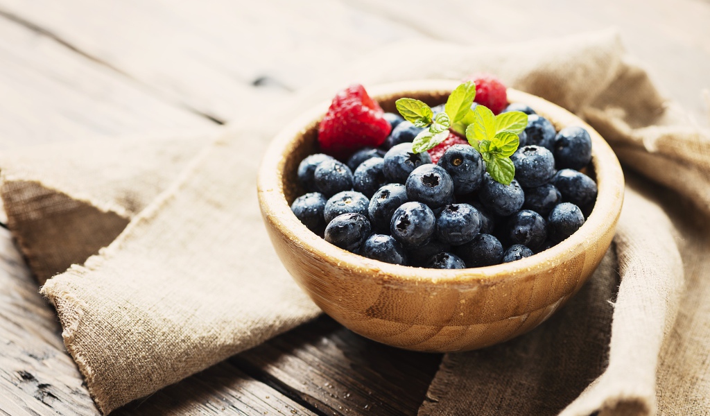 Мокрые ягоды черники в деревянной миске с малиной 