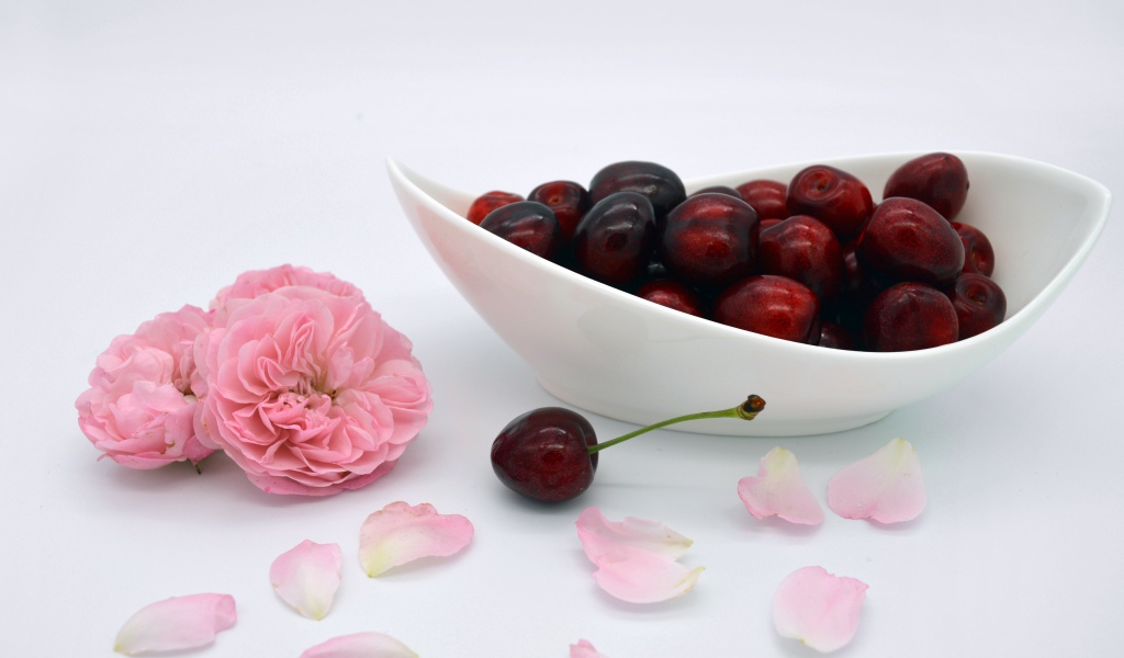 White plate with red cherries on the table with flowers