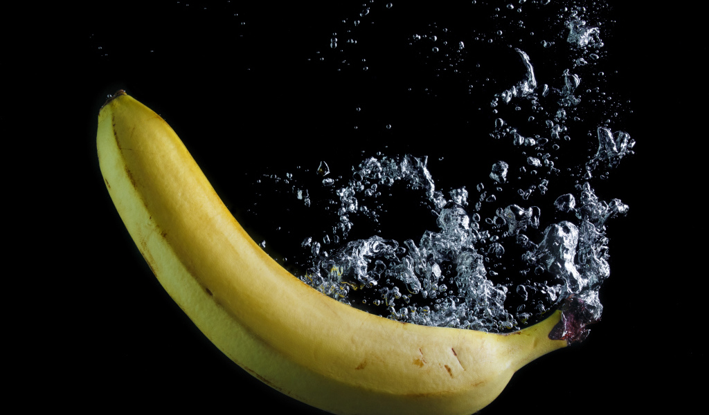 Желтый банан в воде на черном фоне