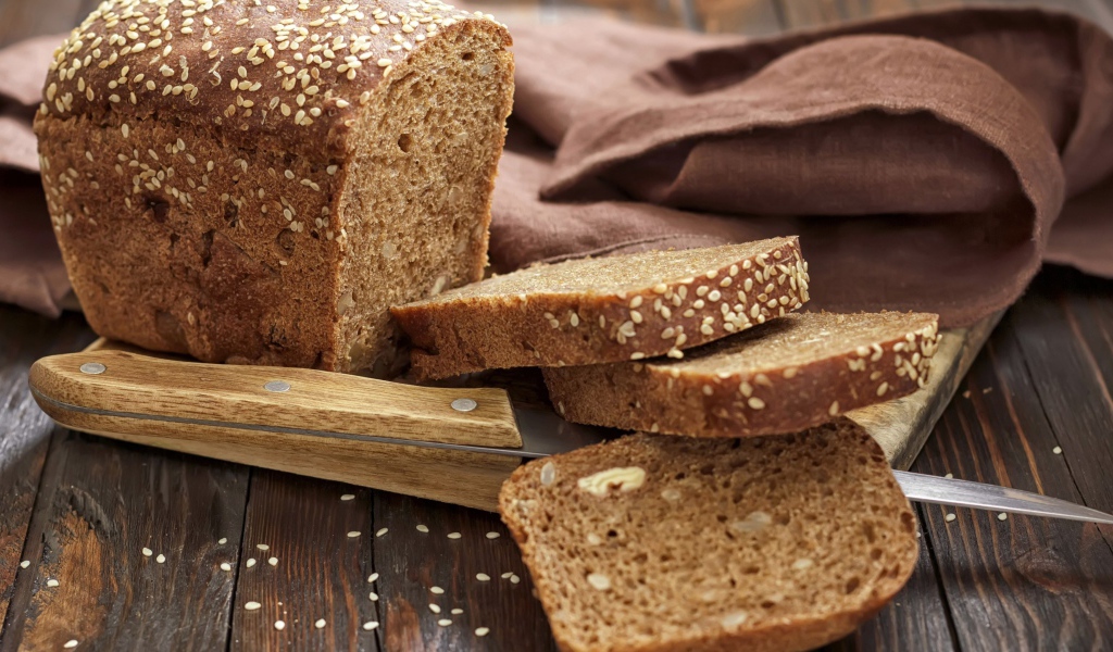 Буханка хлеба нарезанная кусочками на столе с ножом