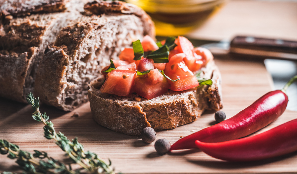 Черный хлеб с кусочками помидора на столе с острым красным перцем