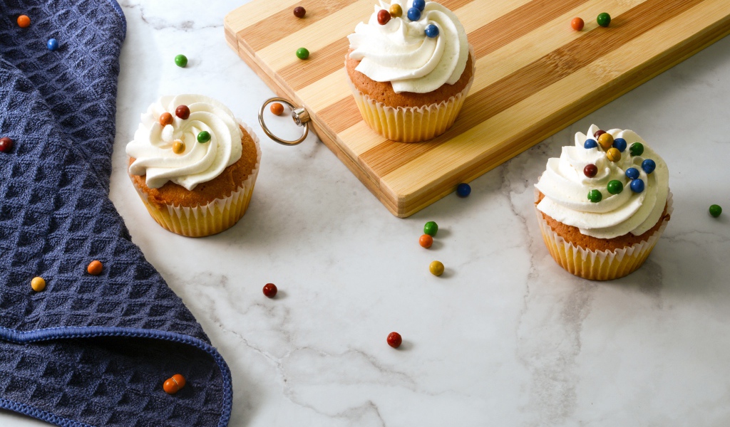 Кексы с кремом и разноцветными шариками на столе с доской