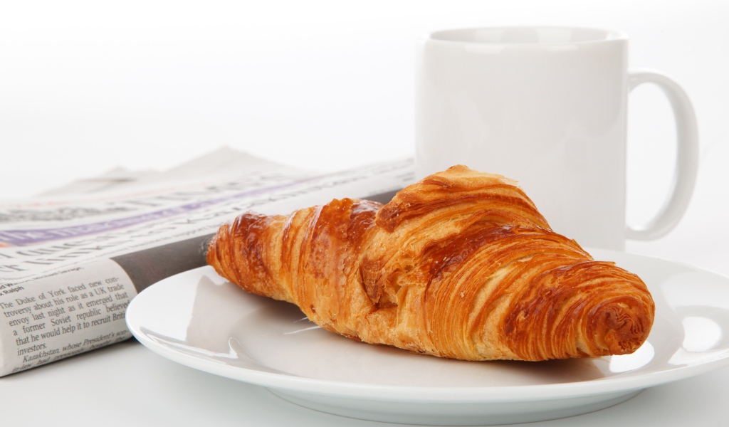 Свежий круассан лежит на белой тарелке с кофе 