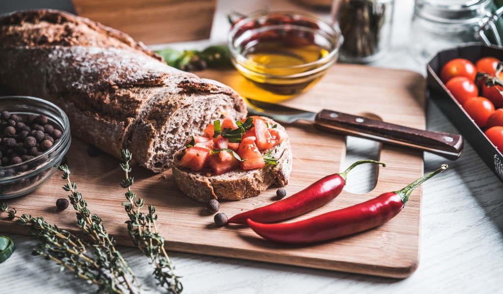 Батон с помидорами и красным перцем на столе с маслом