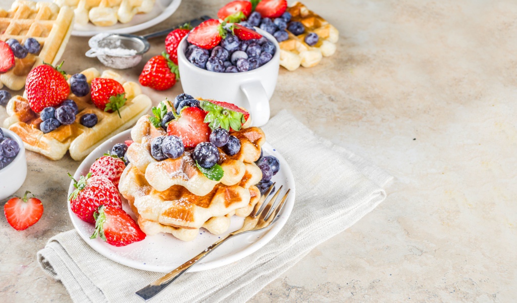 Вкусные сладкие вафли на тарелке с ягодами и сахарной пудрой 