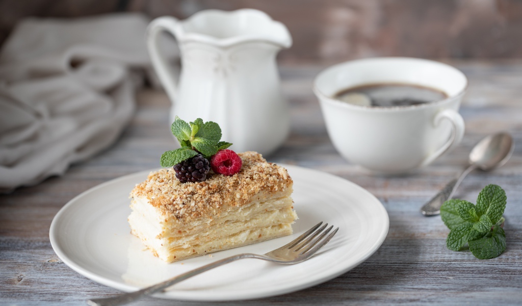 Кусок торта лежит на белой тарелке на столе с кофе