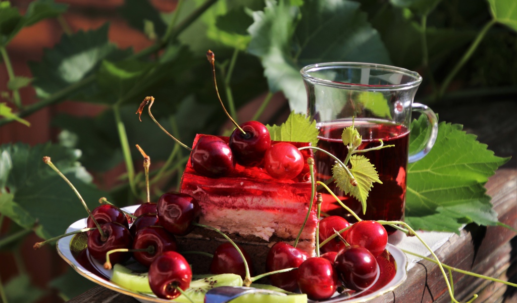 Кусок торта с черешней на столе с чашкой чая 