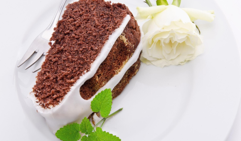 Кусок шоколадного пирога на тарелке с белой розой 