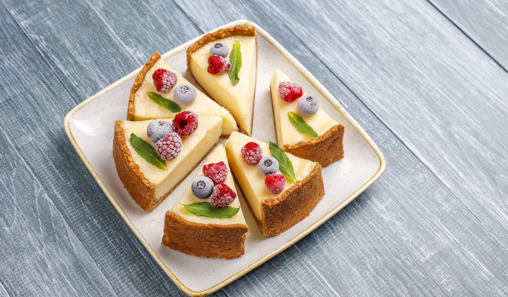 Аппетитный чизкейк с ягодами нарезан кусками на тарелке 