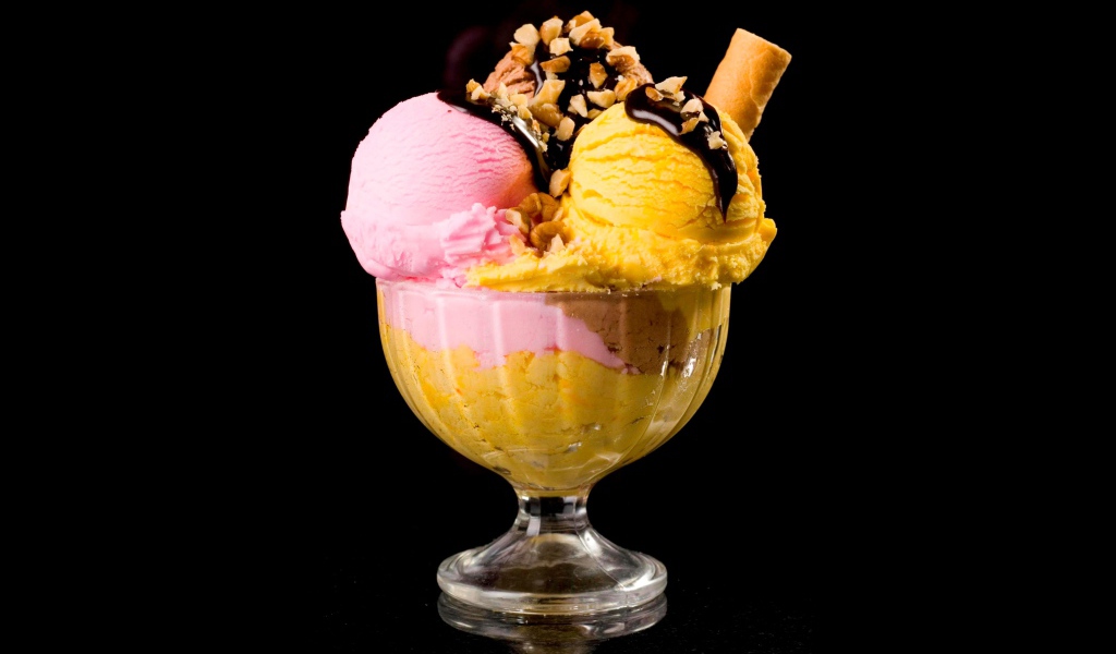 Шарики фруктового мороженого в креманке с орехами и шоколадом на черном фоне